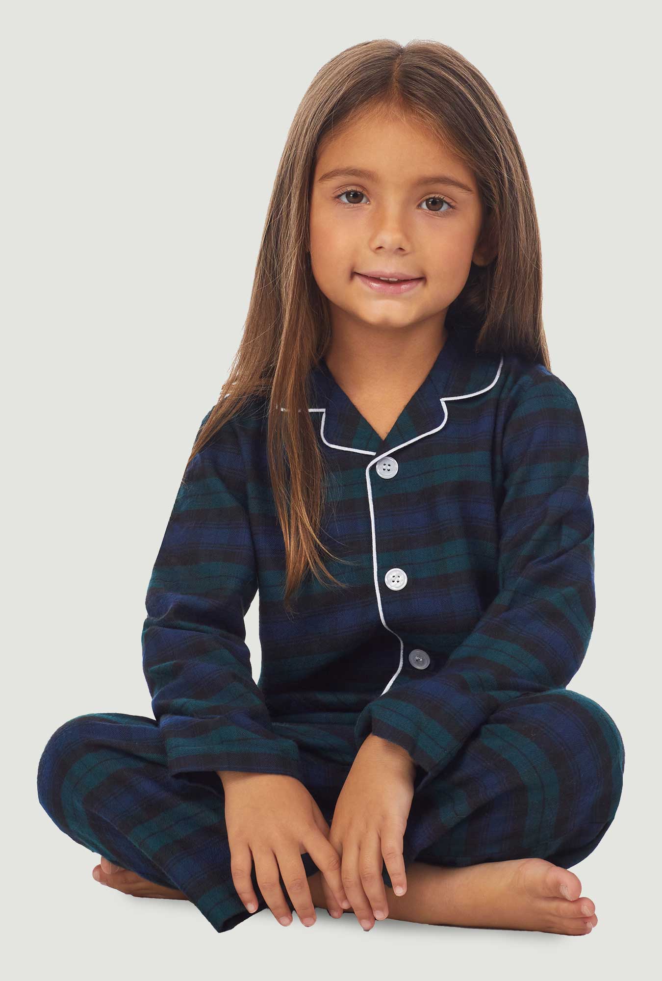 A kid wearing a long sleeve pajama set with black watch plaid pattern.