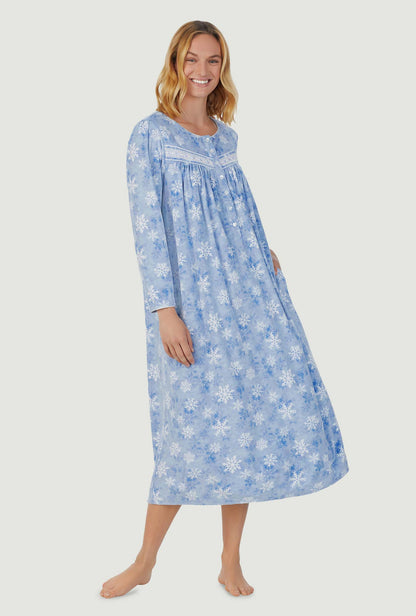 A lady wearing blue long sleeve cozy  fleece gown with snowflake wonderland print.