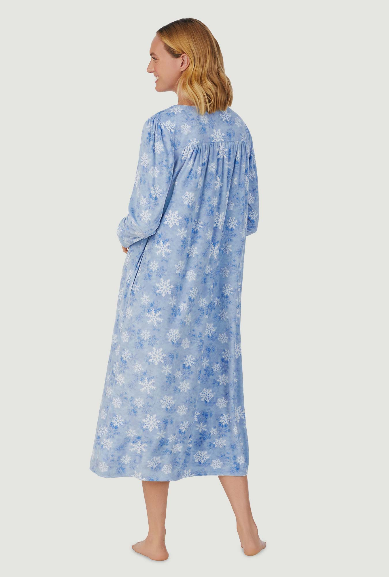 A lady wearing blue long sleeve cozy  fleece gown with snowflake wonderland print.